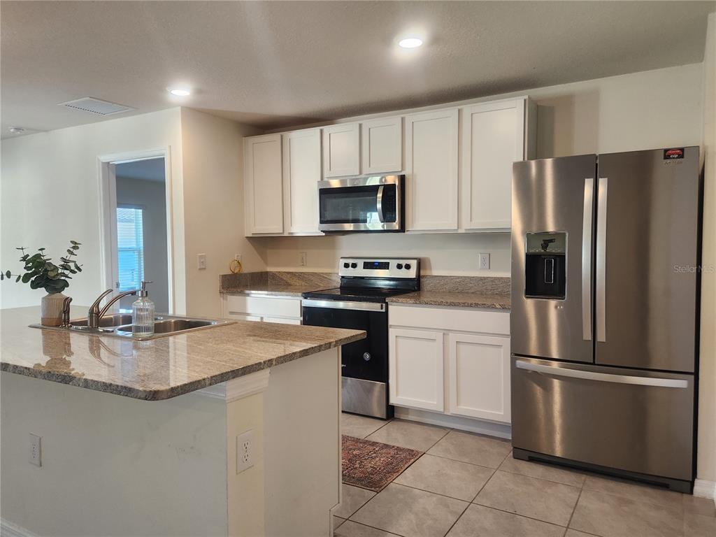 A kitchen features white cabinets, granite countertops, stainless steel appliances, and a central island — 8696 SW 49TH CIRCLE, OCALA, FL