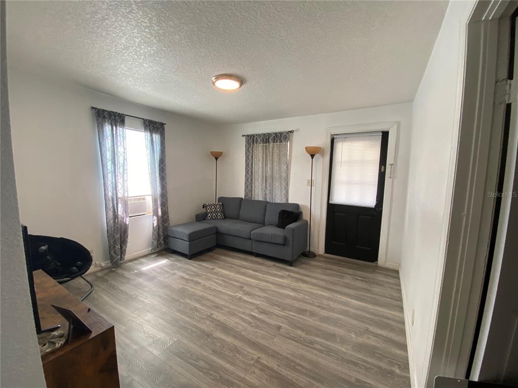 A living room features gray wood-look flooring, a sectional sofa, and a black exterior door — 1835 W GREENWOOD STREET, LAKELAND, FL