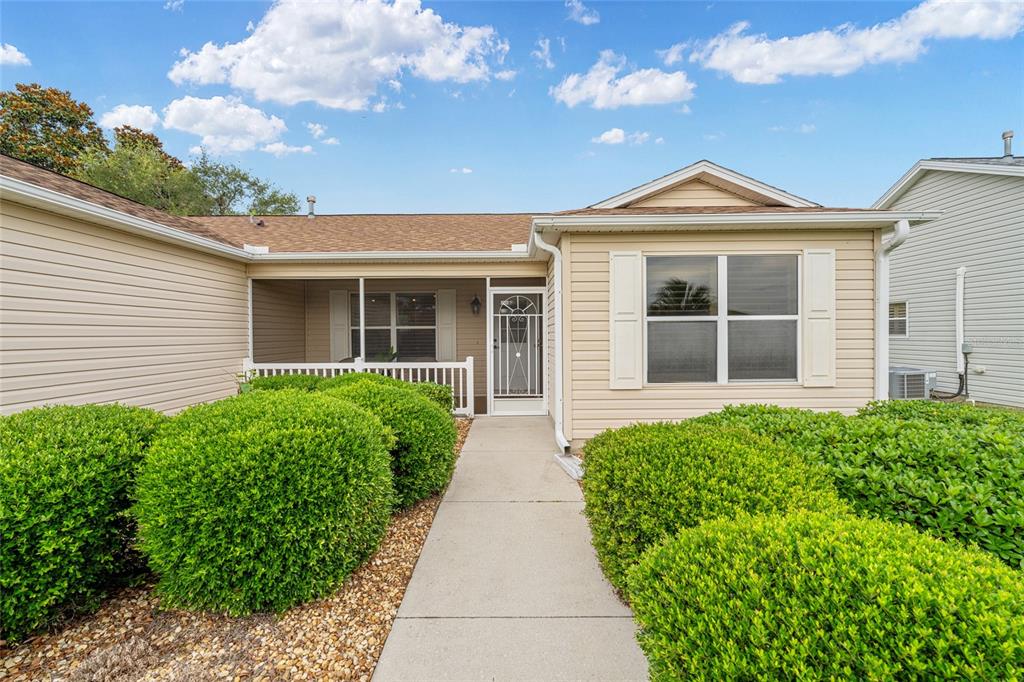 A single-story house with tan siding, a screened front porch, and manicured green bushes — 991 BARRYMOORE LOOP, THE VILLAGES, FL