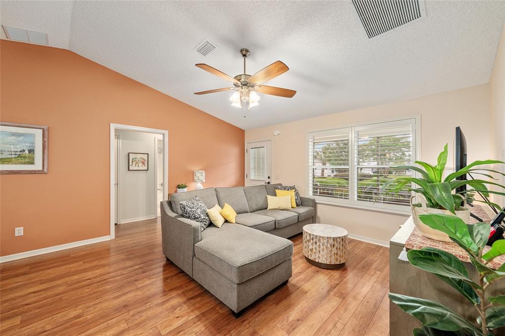 A living room features a grey sectional sofa, wood flooring, and an orange accent wall — 991 BARRYMOORE LOOP, THE VILLAGES, FL