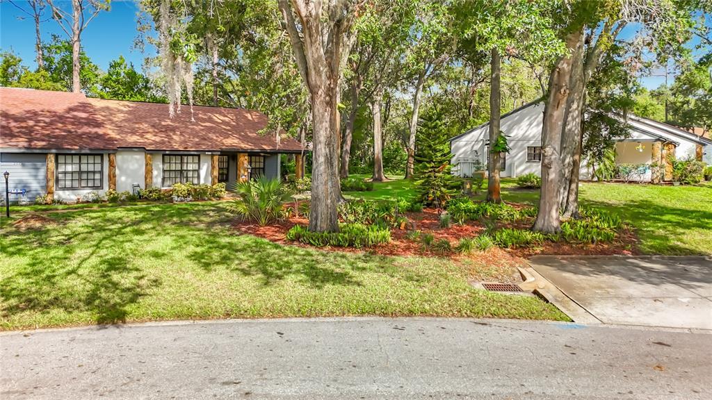 A single-story house with a brown roof sits behind a lawn and mature trees — 2077 WOODCUTTER COURT, SPRING HILL, FL
