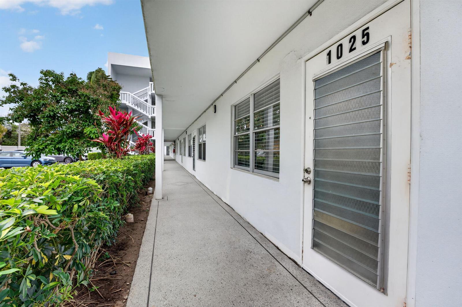 An exterior walkway leads past a row of white apartment doors with louvered glass inserts — 1025 Ventnor # H, Deerfield Beach FL 33442, DEERFIELD BEACH, FL