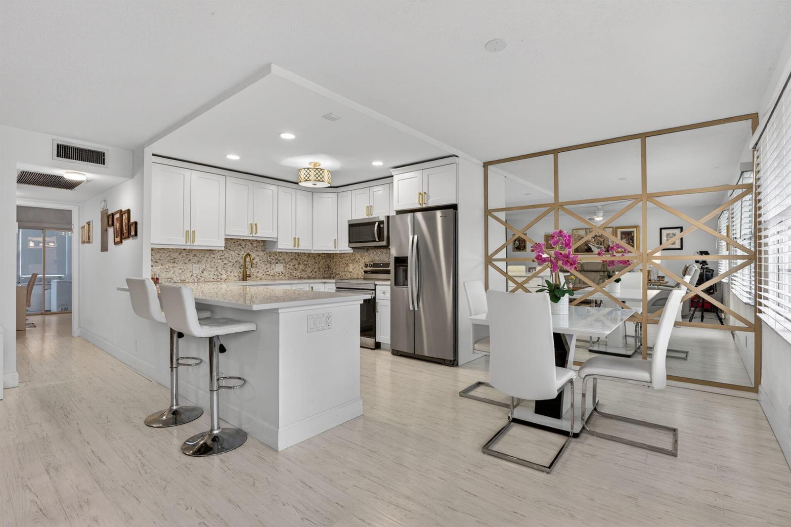 A modern kitchen and dining area with white cabinetry, stainless steel appliances, and mirrored walls — 1025 Ventnor # H, Deerfield Beach FL 33442, DEERFIELD BEACH, FL