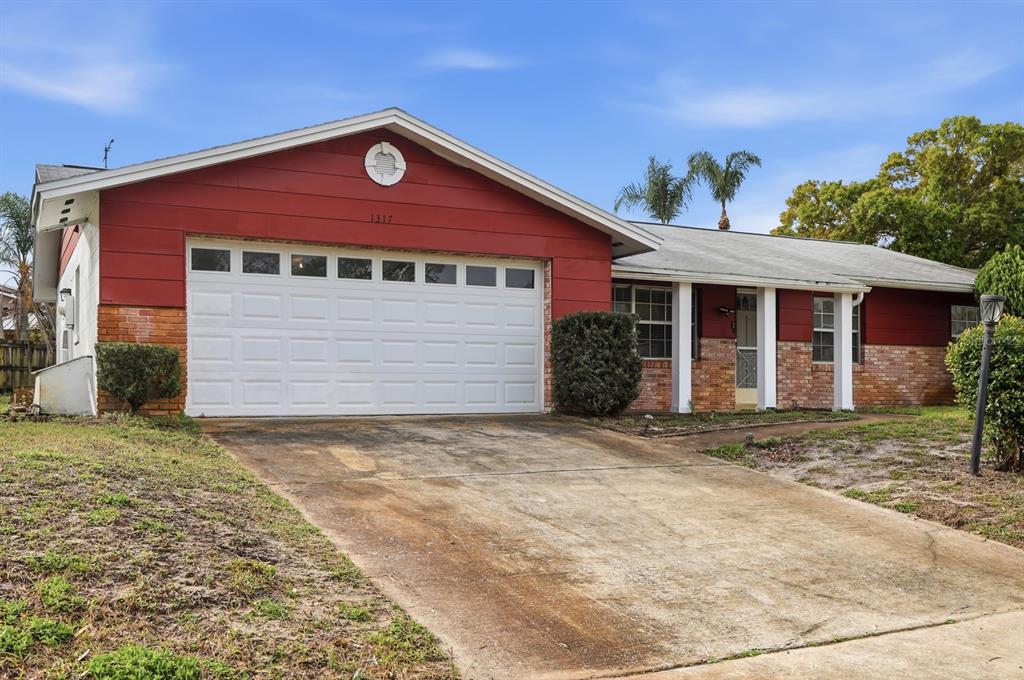 A single-story house with a red facade, brick accents, and a two-car garage — 1317 N SHANGRI LA DRIVE, DAYTONA BEACH, FL