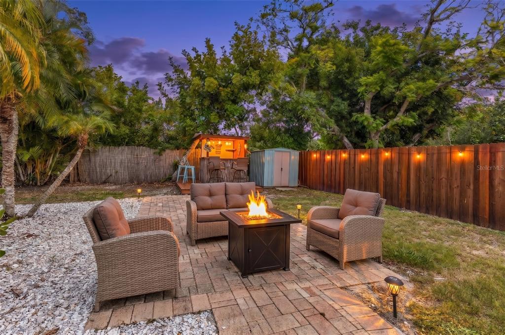 A backyard patio features a fire pit, wicker furniture, a wooden fence, and a tiki bar — 1664 LAKEVIEW PLACE, ENGLEWOOD, FL