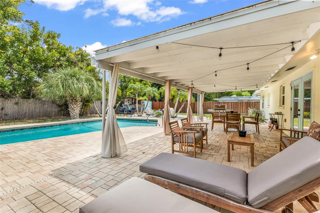 A covered patio with brick pavers overlooks a swimming pool and a fenced backyard — 1664 LAKEVIEW PLACE, ENGLEWOOD, FL