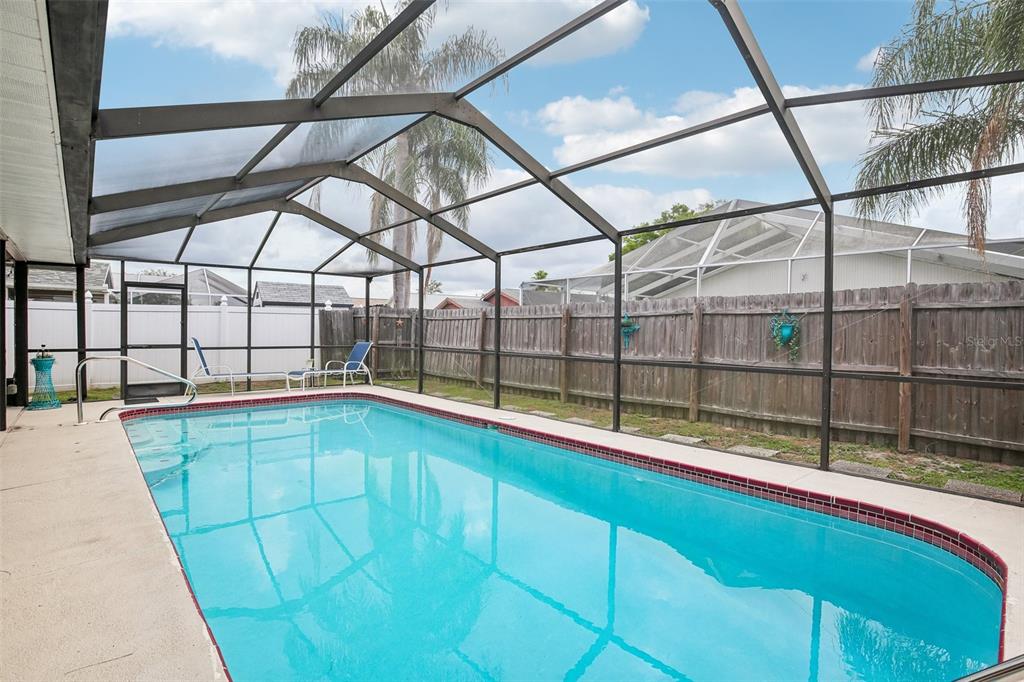 A rectangular swimming pool enclosed by a screened lanai with a wooden fence in the background — 12630 CEDAR RIDGE DRIVE, HUDSON, FL