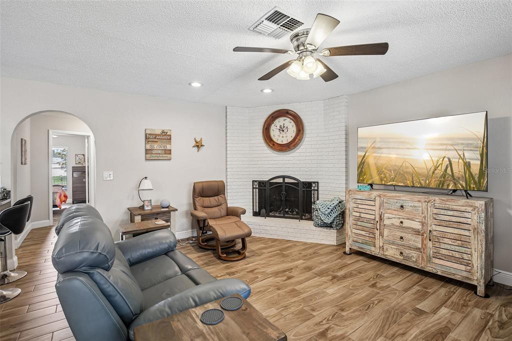 A living room features a white brick corner fireplace, a television, and wood-look tile flooring — 12630 CEDAR RIDGE DRIVE, HUDSON, FL