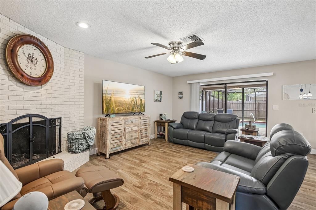 A living room features a white brick fireplace, gray leather furniture, and wood-look flooring — 12630 CEDAR RIDGE DRIVE, HUDSON, FL
