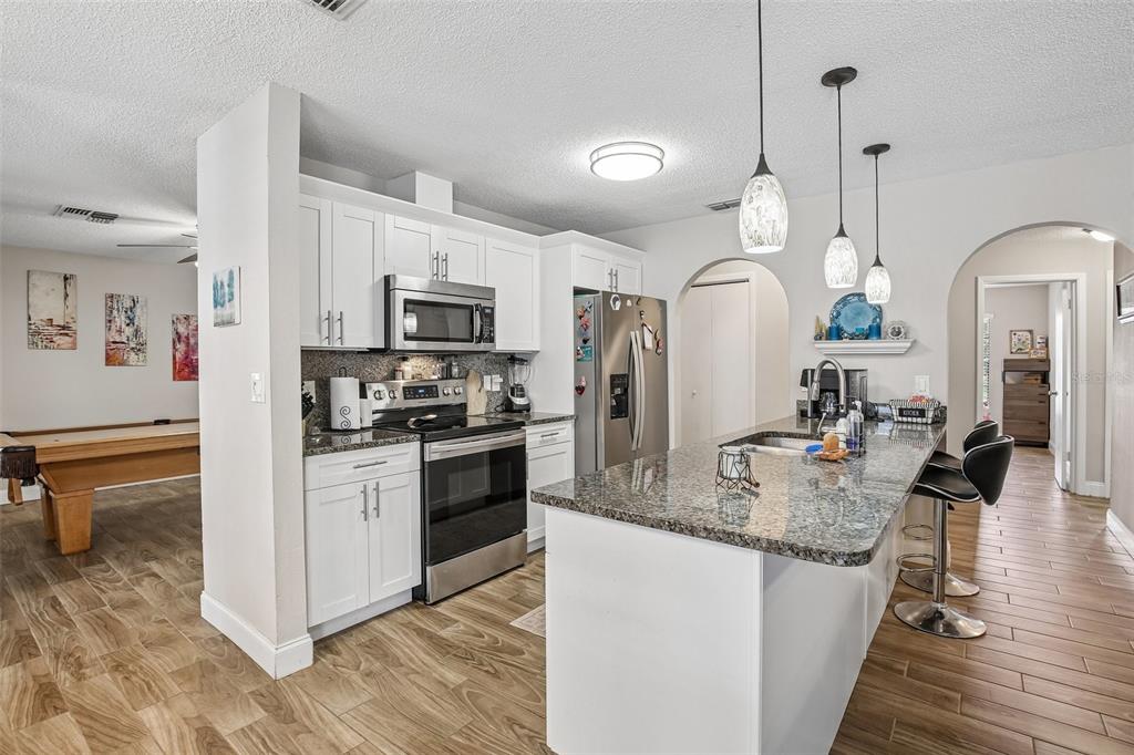A kitchen features white cabinets, stainless steel appliances, a granite island, and wood-look tile flooring — 12630 CEDAR RIDGE DRIVE, HUDSON, FL