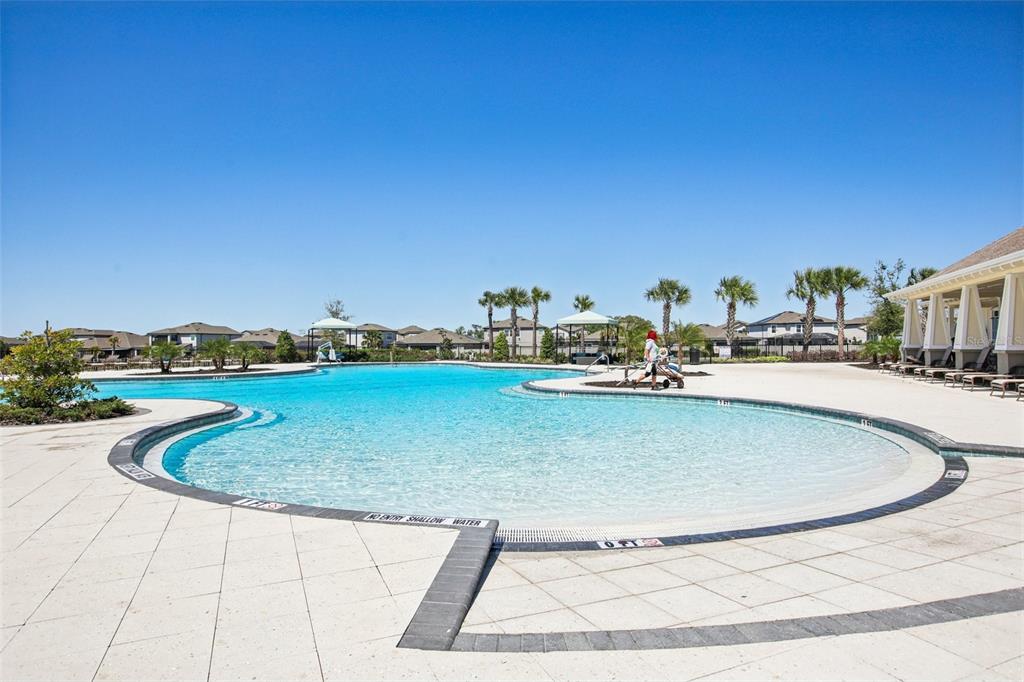 A large outdoor swimming pool with a zero-entry area and surrounding patio under a clear sky — 11218 SAGE CANYON DRIVE, RIVERVIEW, FL
