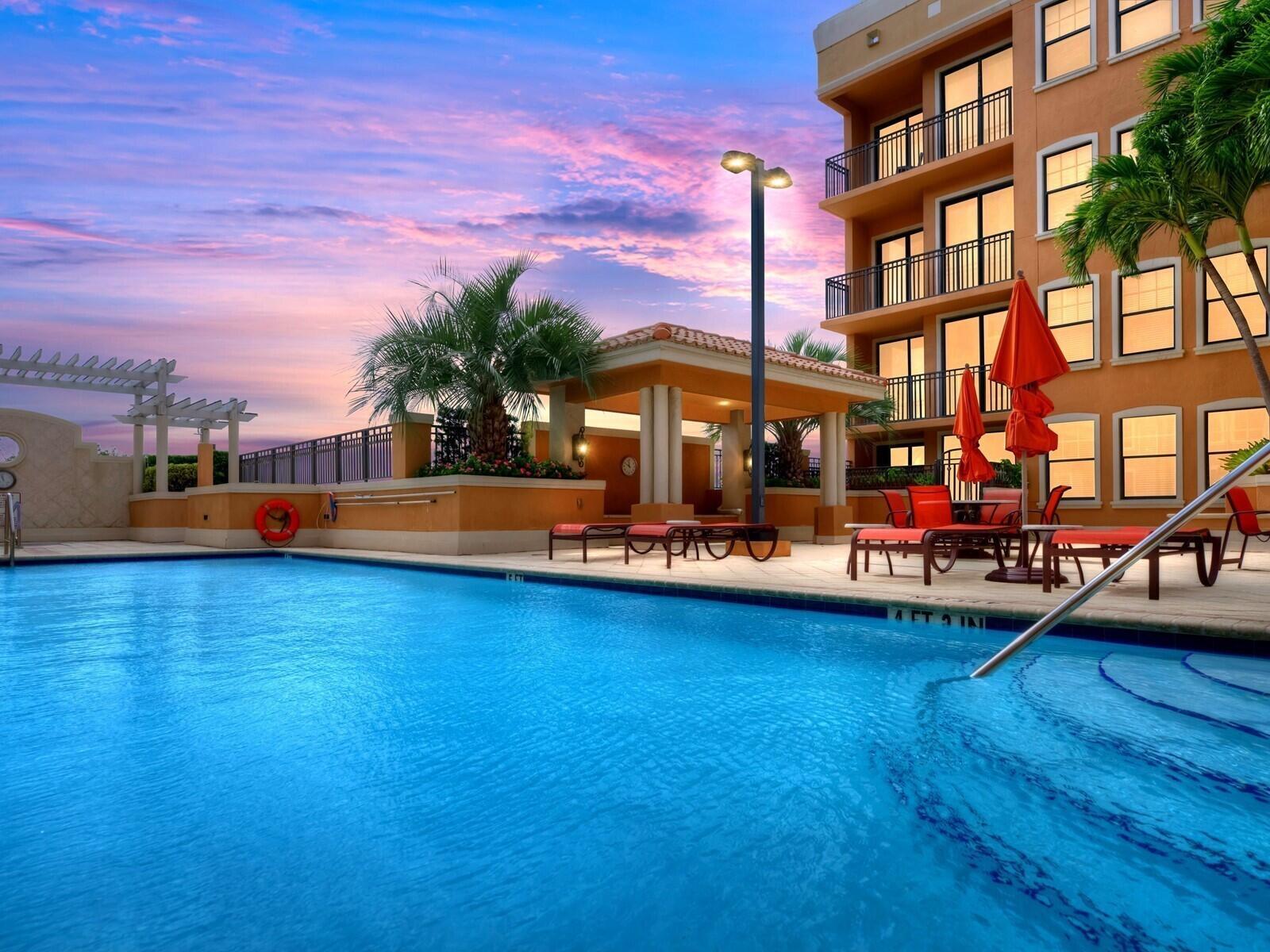 A swimming pool with lounge chairs and umbrellas sits beside a multi-story apartment building — 511 Lucerne Avenue # 316, FL 33460, FL