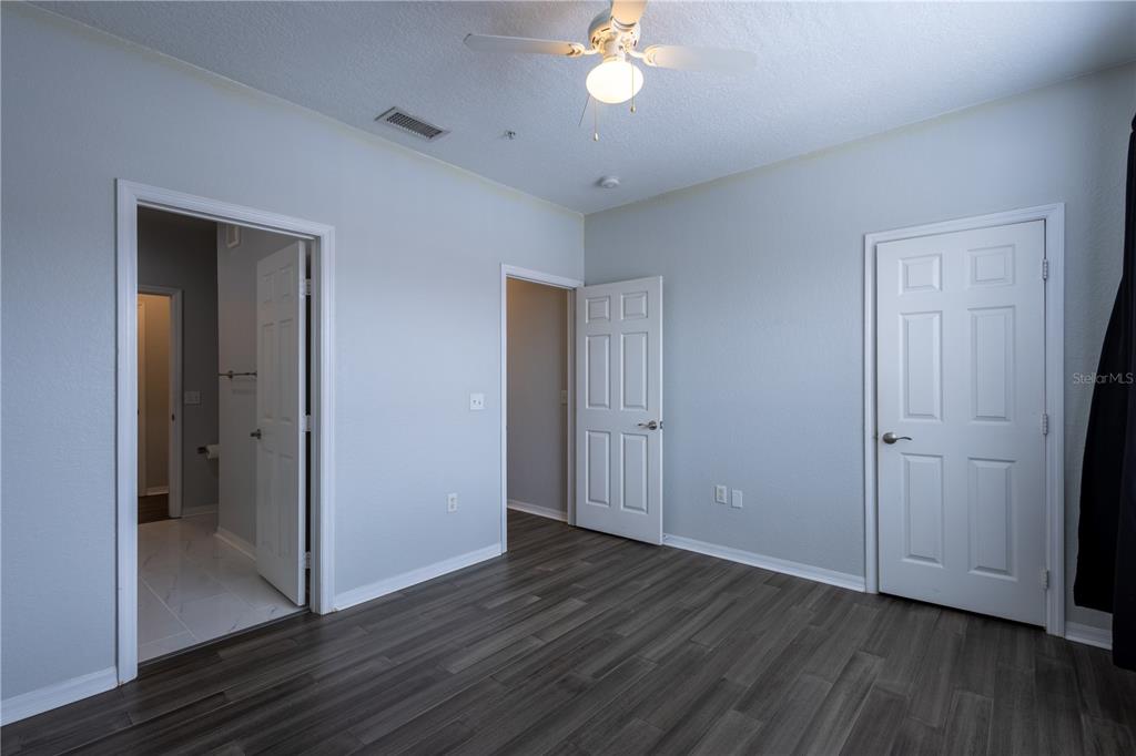A bedroom with light blue walls, dark wood-look flooring, a ceiling fan, and three doors — 18001 RICHMOND PLACE DRIVE UNIT 427, TAMPA, FL