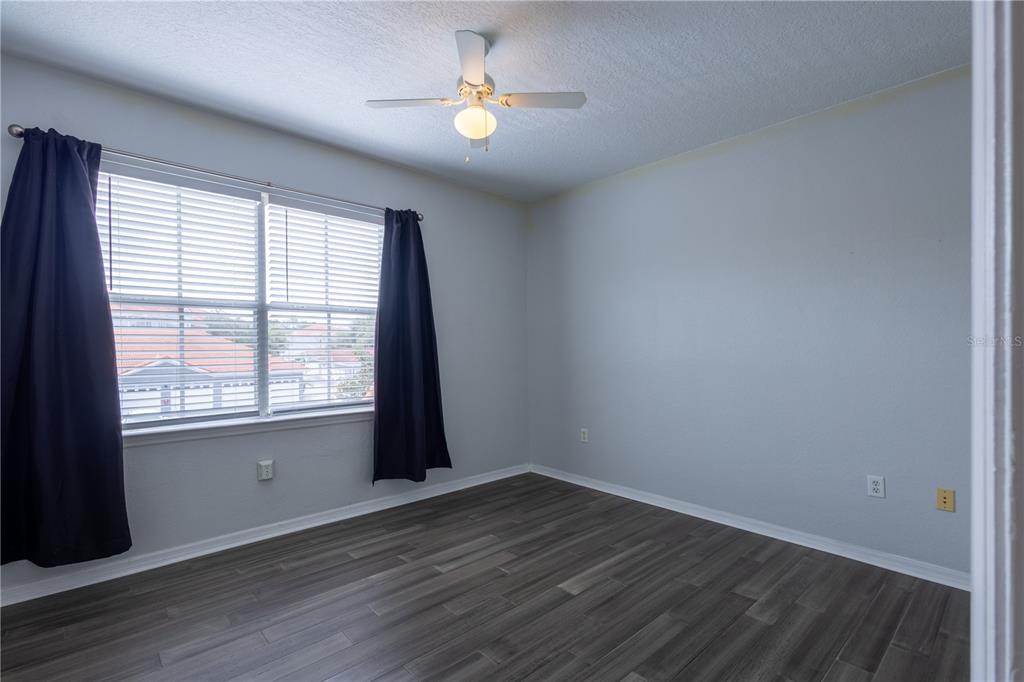 An empty bedroom features gray walls, dark wood-look flooring, a ceiling fan, and window curtains — 18001 RICHMOND PLACE DRIVE UNIT 427, TAMPA, FL