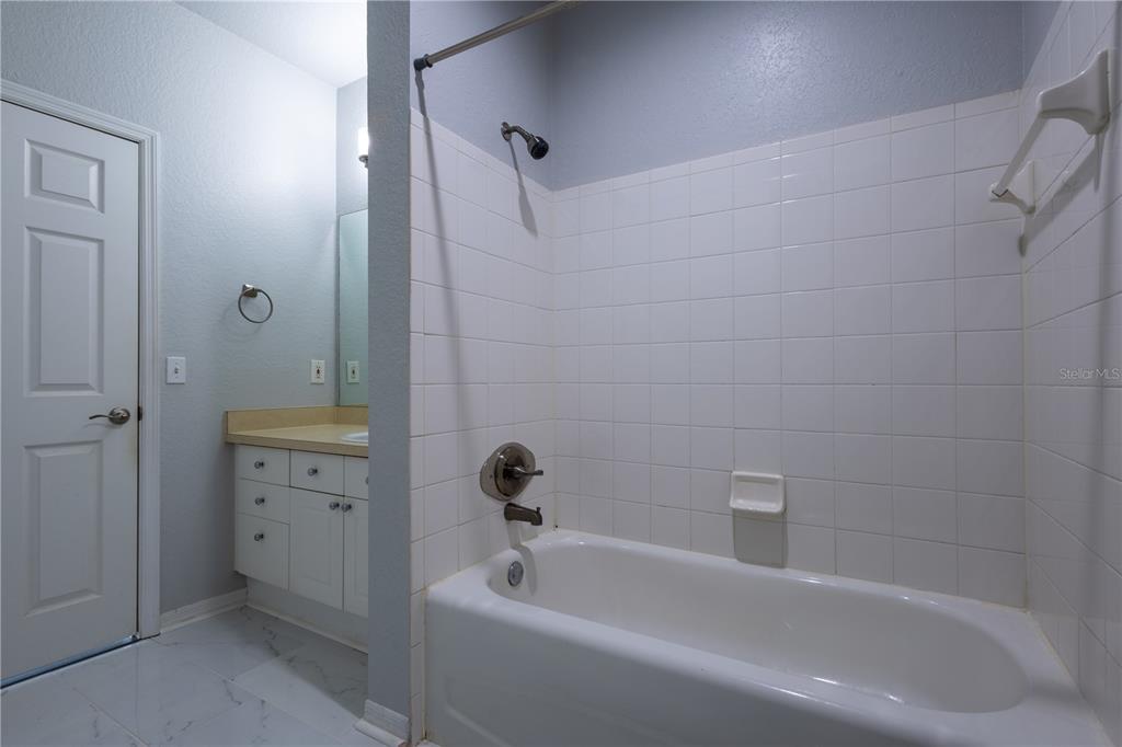 A bathroom features a white tiled shower-tub combination, a vanity with a mirror, and light-colored walls — 18001 RICHMOND PLACE DRIVE UNIT 427, TAMPA, FL
