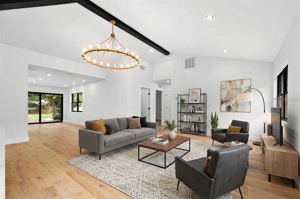A bright living room features light wood floors, a vaulted ceiling, and a large chandelier — 605 N WOODLYNNE AVENUE, TAMPA, FL