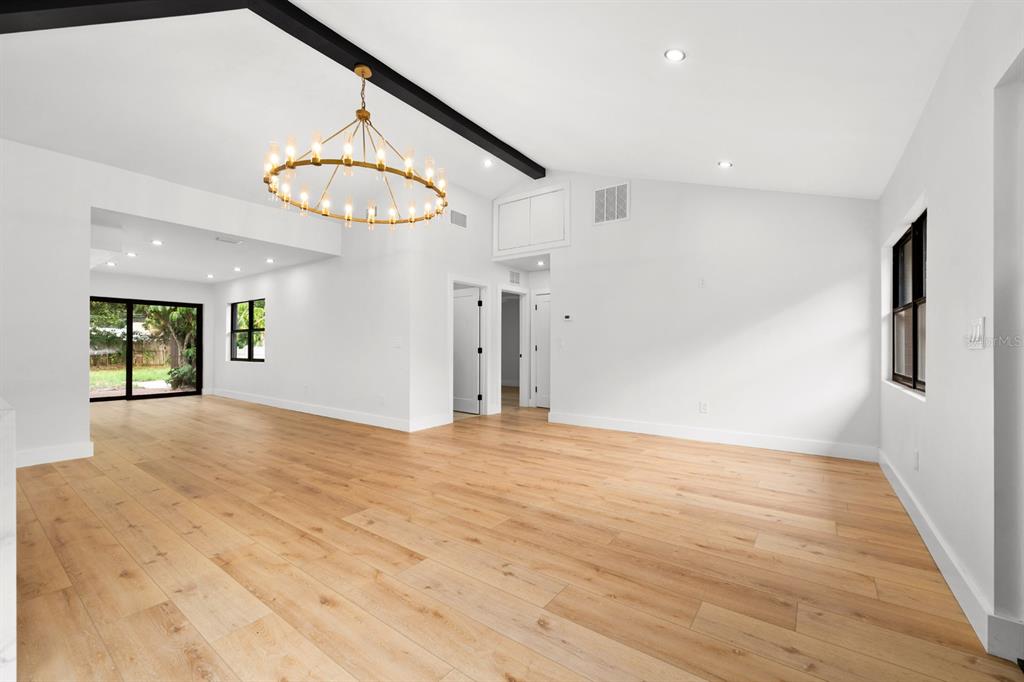 A bright, open-concept living area features light wood flooring, a black ceiling beam, and chandelier — 605 N WOODLYNNE AVENUE, TAMPA, FL