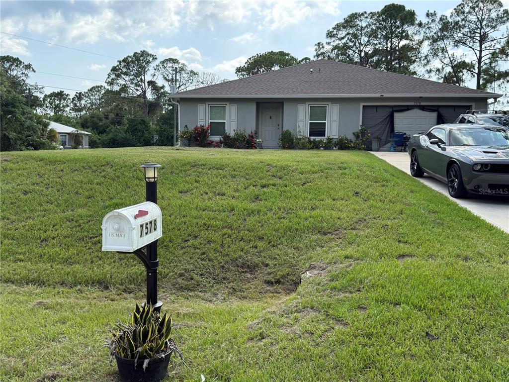 A single-story house with a gray exterior, a front lawn, and a driveway with a car — 7578 TASCO DRIVE, NORTH PORT, FL