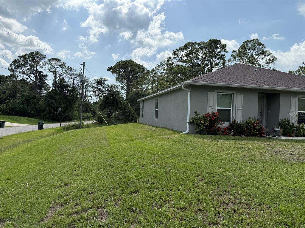 A side view of a gray house with a lawn and trees under a cloudy sky — 7578 TASCO DRIVE, NORTH PORT, FL