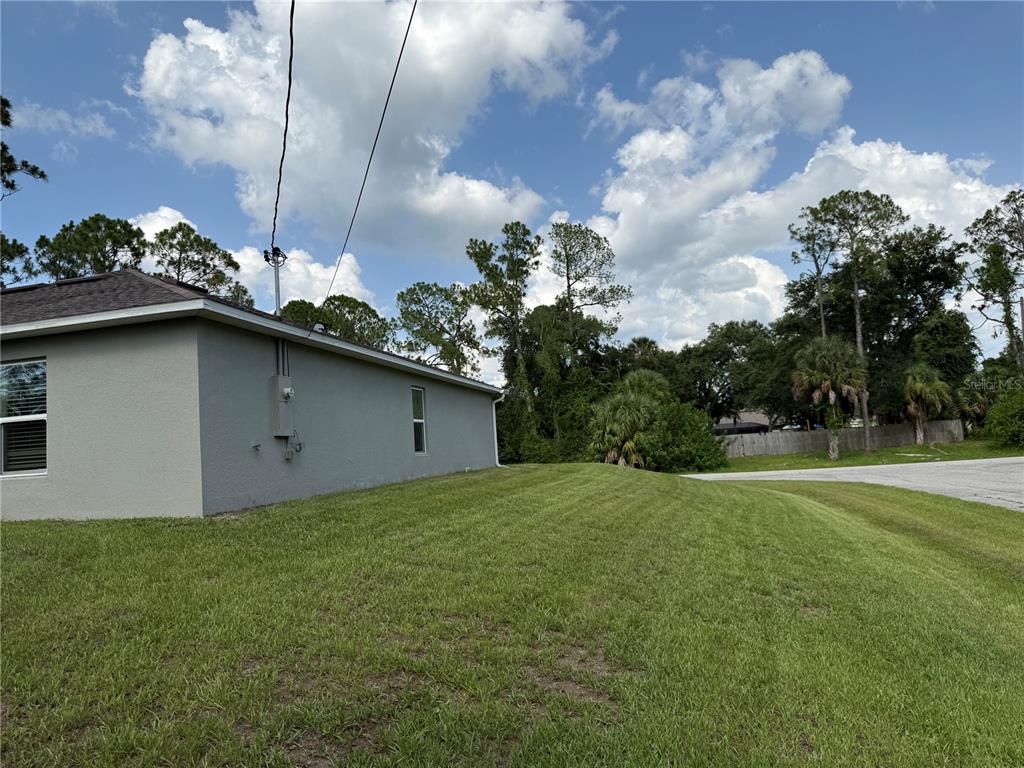 A side view of a gray house exterior with a grassy lawn and surrounding trees — 7578 TASCO DRIVE, NORTH PORT, FL
