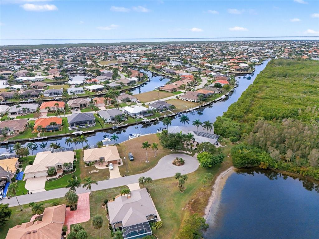 An aerial view shows waterfront homes along a canal with a cul-de-sac and vegetation — 1247 PINE SISKIN DRIVE, PUNTA GORDA, FL