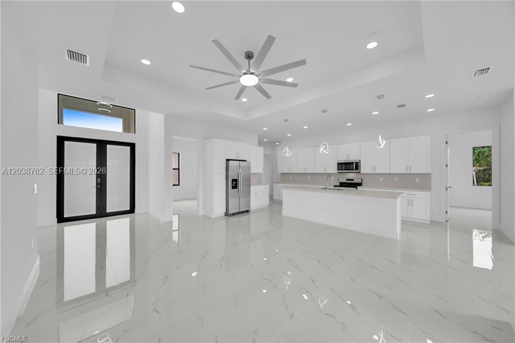 A modern, open-concept kitchen and living area features white cabinetry, marble-look tile floors, and recessed lighting — 3316 7th St SW, Lehigh Acres FL 33976, LEHIGH ACRES, FL