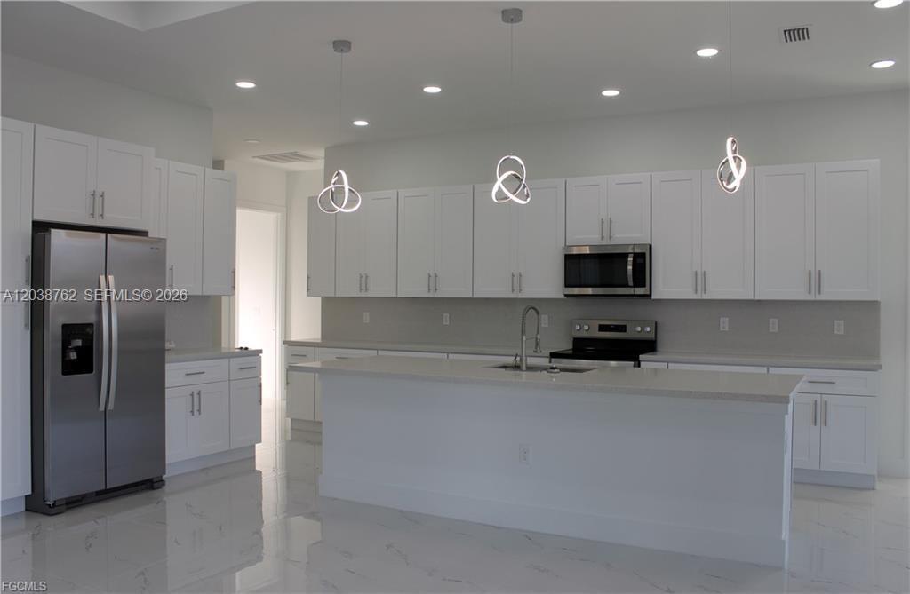 A modern kitchen features white cabinetry, stainless steel appliances, a center island, and tile flooring — 3316 7th St SW, Lehigh Acres FL 33976, LEHIGH ACRES, FL