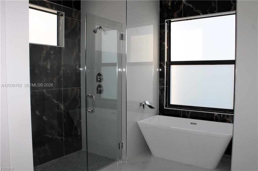 A modern bathroom features a glass-enclosed shower and a freestanding white bathtub — 3316 7th St SW, Lehigh Acres FL 33976, LEHIGH ACRES, FL