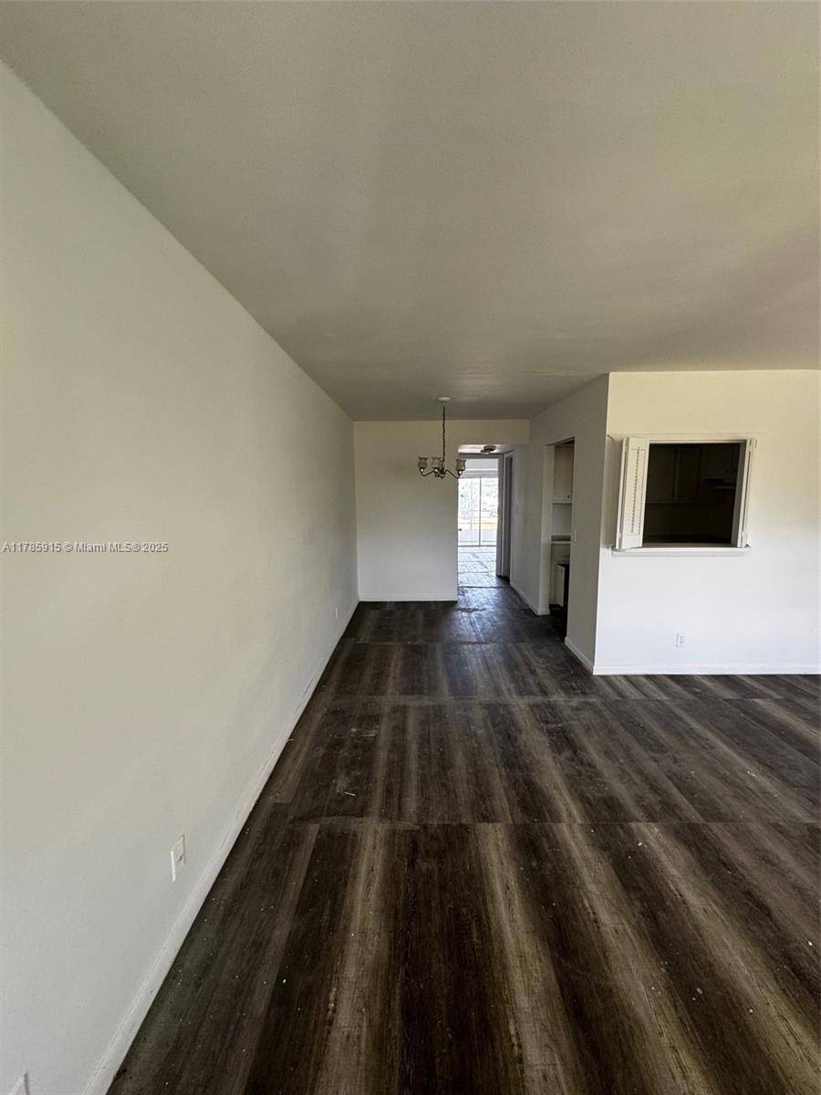 An empty room features dark wood-look flooring, white walls, and a pass-through window — 42 Sheffield B # B, West Palm Beach FL 33417, WEST PALM BEACH, FL