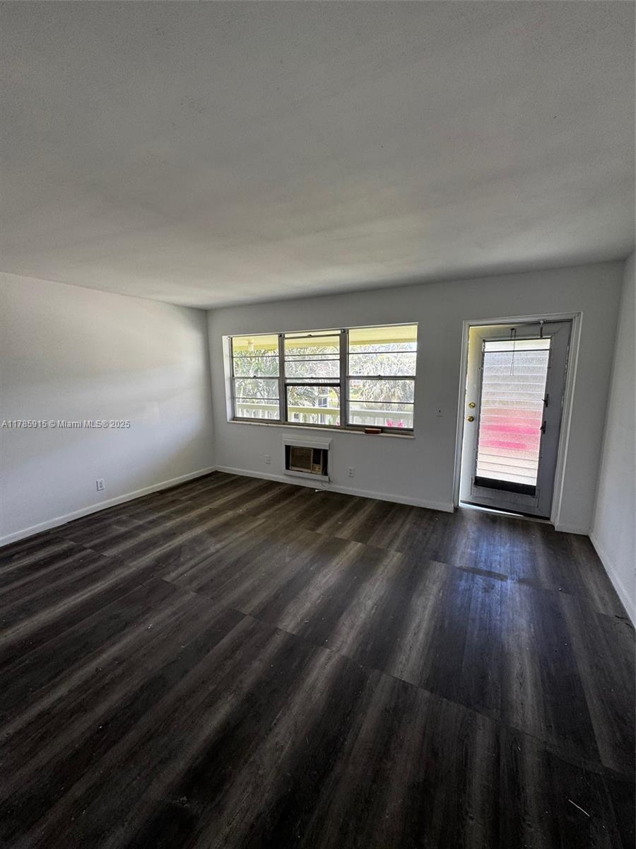 An empty room features dark wood-look flooring, white walls, a window, and a glass door — 42 Sheffield B # B, West Palm Beach FL 33417, WEST PALM BEACH, FL
