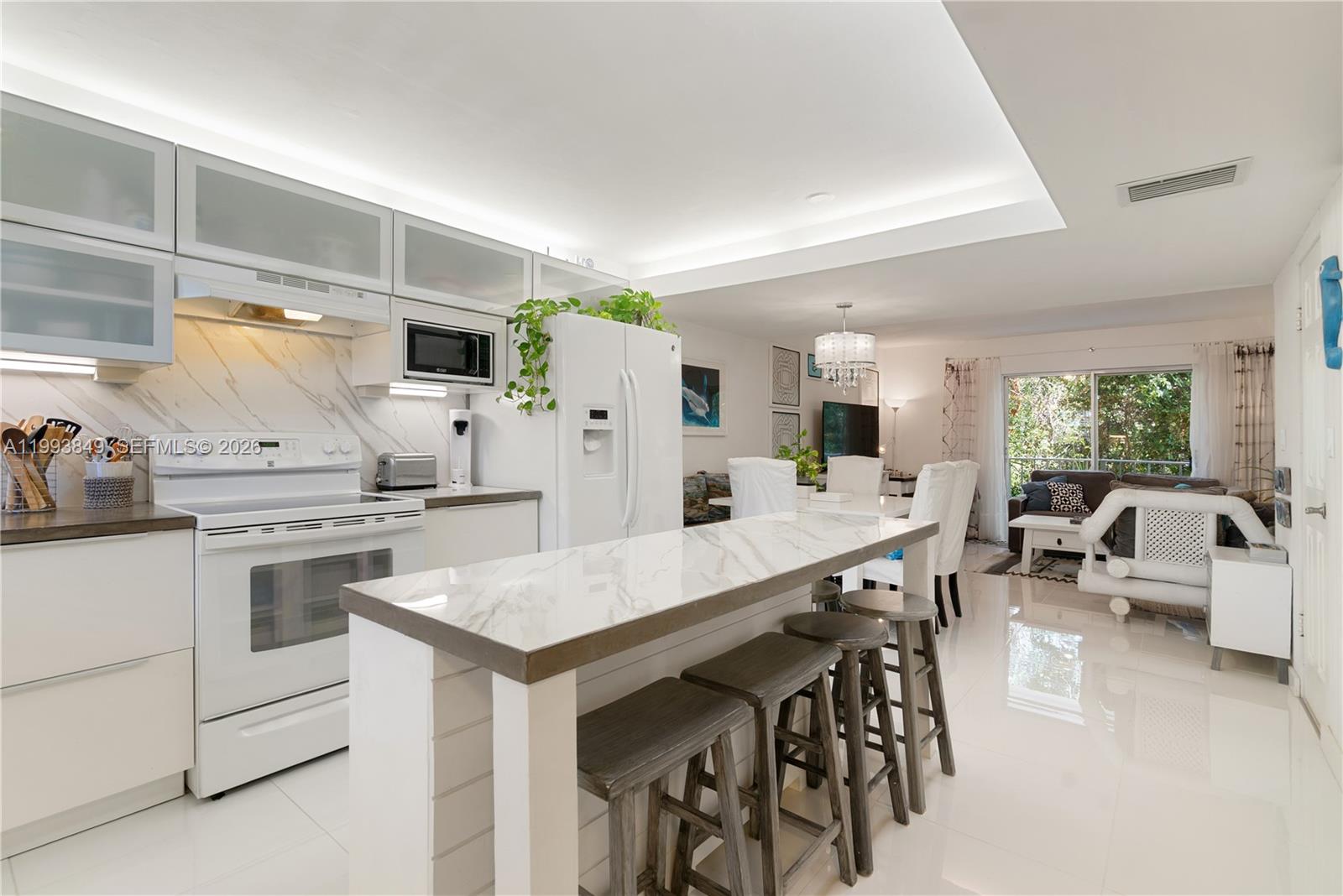 A modern kitchen with white cabinetry and a marble-topped island opens into a living area — 300 Ocean Dr # 26, Key Largo FL 33037, KEY LARGO, FL