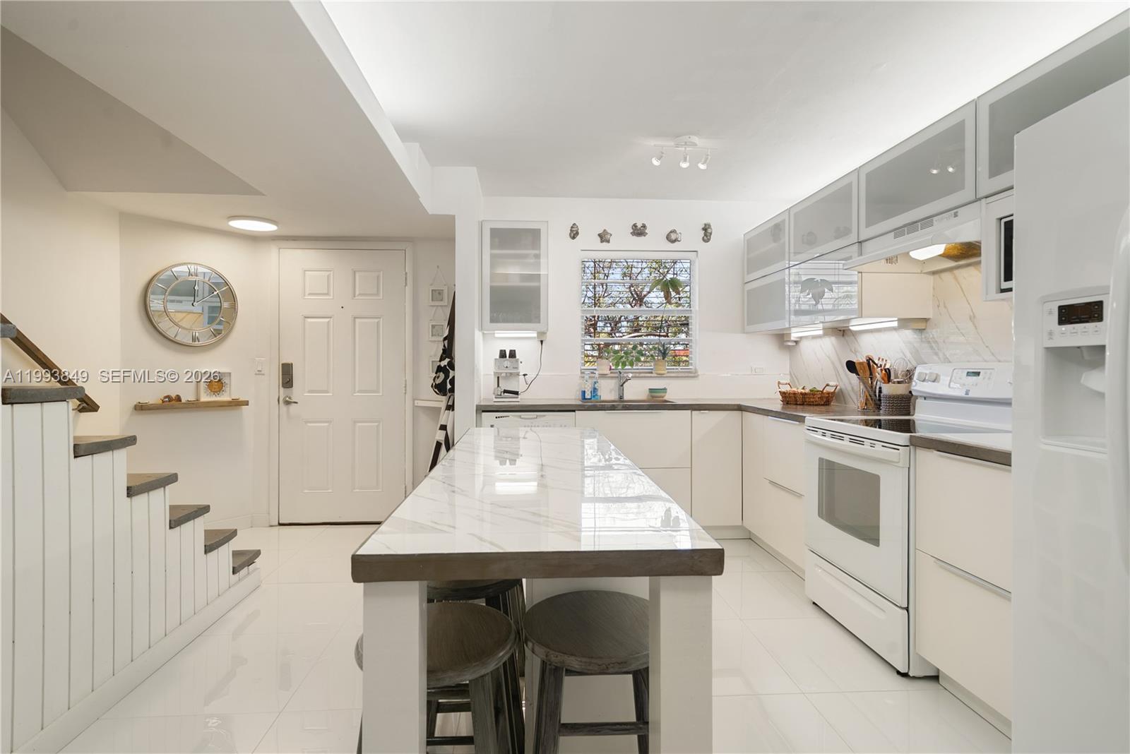 A modern kitchen features white cabinetry, a marble-topped island, and a staircase on the left — 300 Ocean Dr # 26, Key Largo FL 33037, KEY LARGO, FL