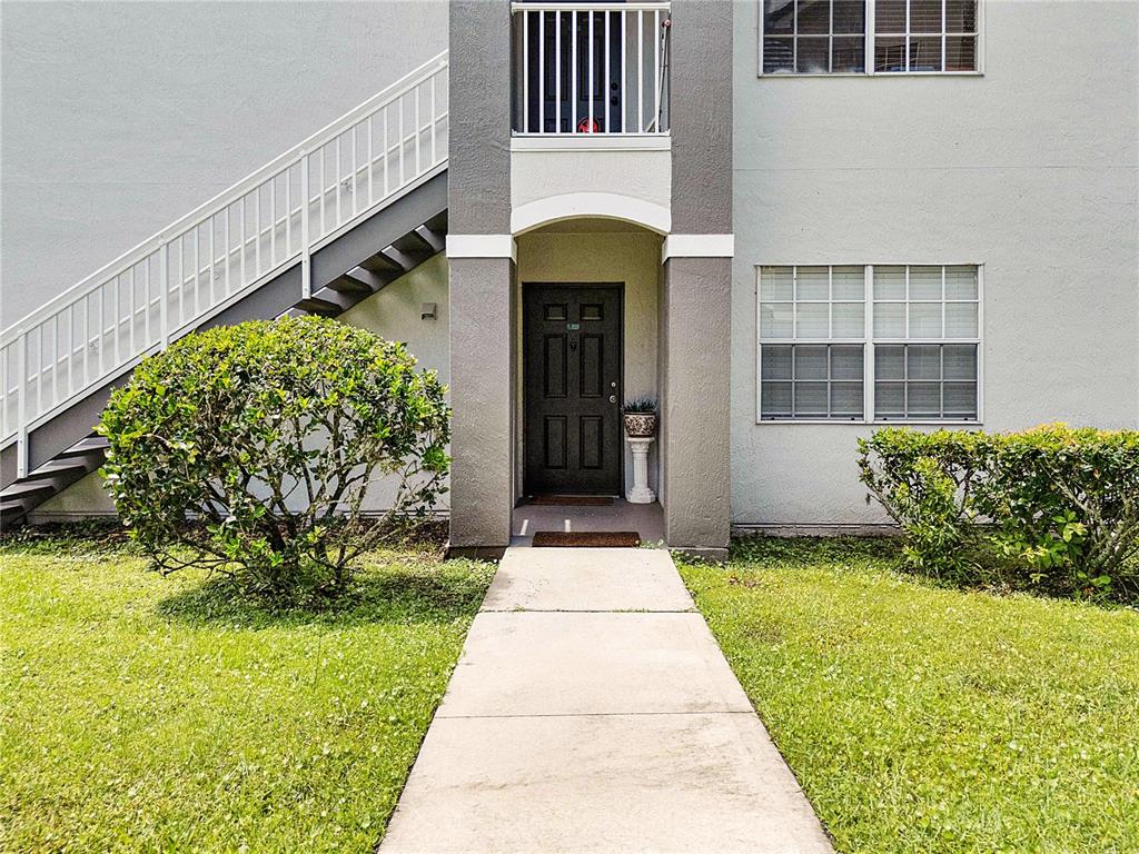 A concrete walkway leads to the dark front door of a two-story apartment building — 13929 FAIRWAY ISLAND DRIVE UNIT 818, ORLANDO, FL