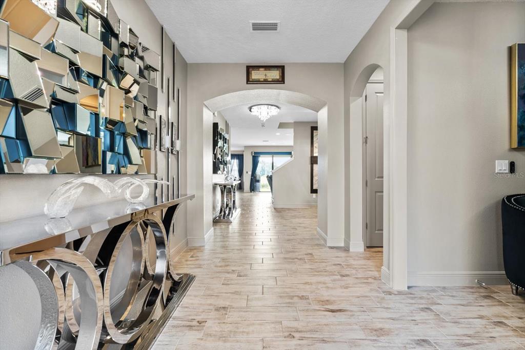 A tiled hallway features a mirrored console table, wall art, and an arched entryway — 12854 BOGGY CREEK DRIVE, RIVERVIEW, FL