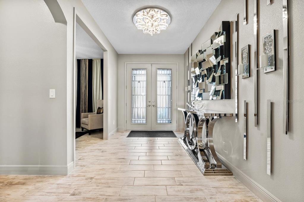 A bright entryway features light wood-look tile floors, a crystal chandelier, and a mirrored console — 12854 BOGGY CREEK DRIVE, RIVERVIEW, FL