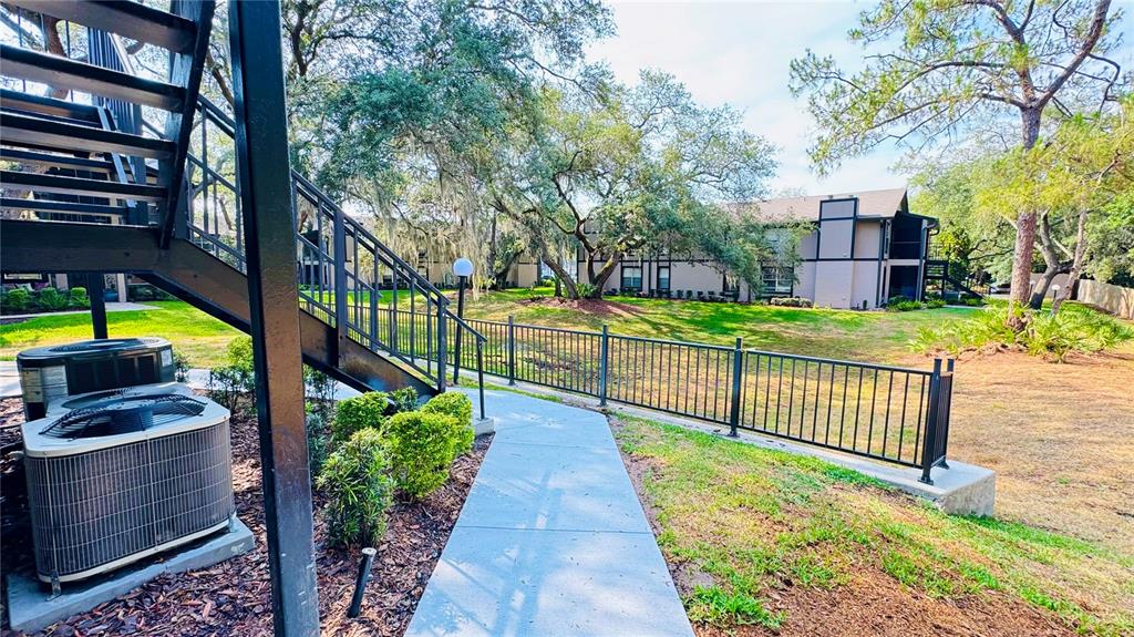 A concrete walkway leads past an air conditioning unit toward apartment buildings and trees — 4032 TUMBLE WOOD TRAIL UNIT 104, TAMPA, FL