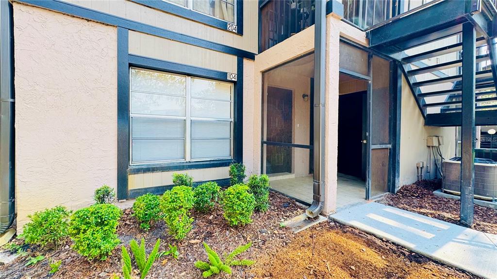 The exterior of a multi-story apartment building features a screened-in entryway and metal stairs — 4032 TUMBLE WOOD TRAIL UNIT 104, TAMPA, FL