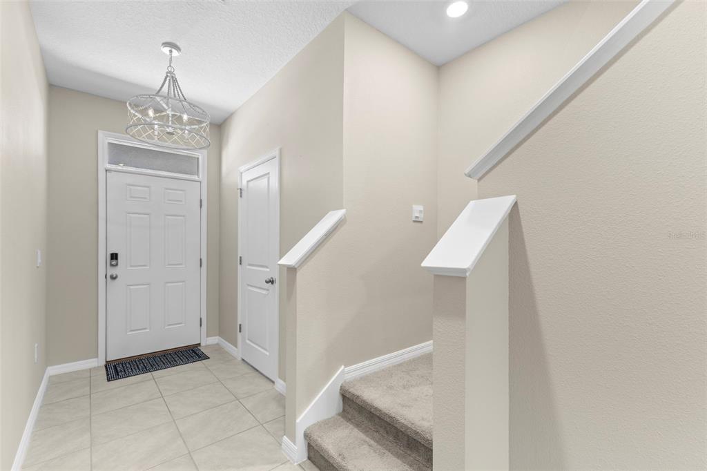 An entryway features a white front door, a chandelier, and carpeted stairs with white railings — 2908 EVERGREEN ELM PASS, WESLEY CHAPEL, FL