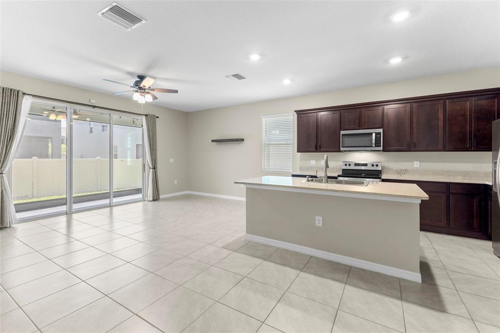 An open-concept kitchen with dark wood cabinets, granite countertops, and tile flooring — 2908 EVERGREEN ELM PASS, WESLEY CHAPEL, FL