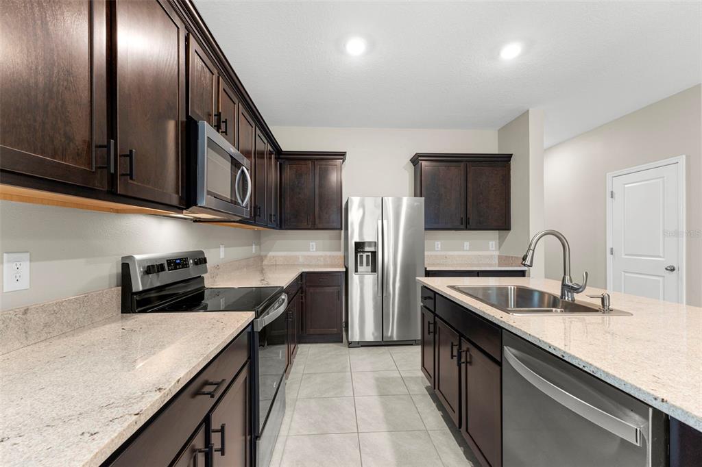A kitchen with dark wood cabinets, stainless steel appliances, and light granite countertops — 2908 EVERGREEN ELM PASS, WESLEY CHAPEL, FL