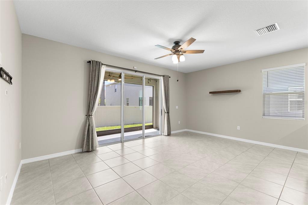 A living room with light tile flooring, a ceiling fan, sliding glass doors, and a shelf — 2908 EVERGREEN ELM PASS, WESLEY CHAPEL, FL