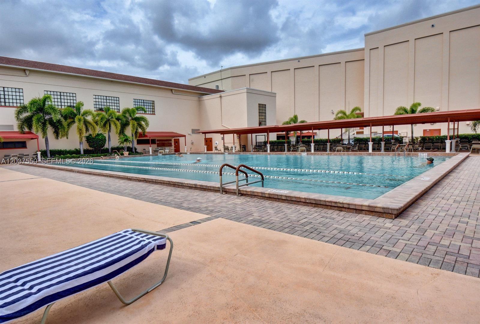 An outdoor swimming pool with lap lanes is surrounded by a paved deck and buildings — 161 Mansfield D # 161, Boca Raton FL 33434, BOCA RATON, FL