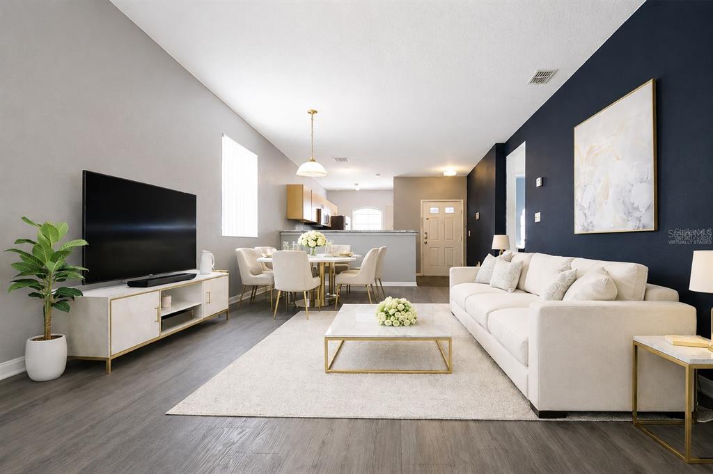 This living and dining room features dark wood-look flooring, a navy accent wall, and furniture — 15201 INDIAN CREEK DRIVE UNIT B, KISSIMMEE, FL