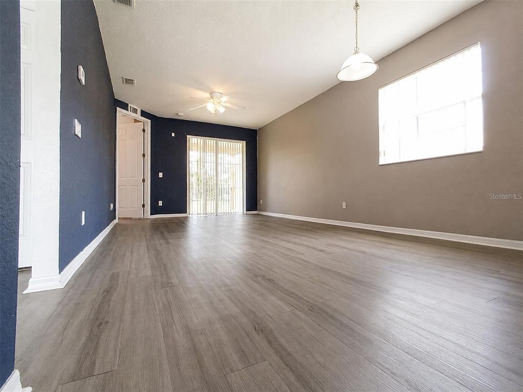 An empty living room features gray wood-look flooring, a dark blue accent wall, and sliding doors — 15201 INDIAN CREEK DRIVE UNIT B, KISSIMMEE, FL