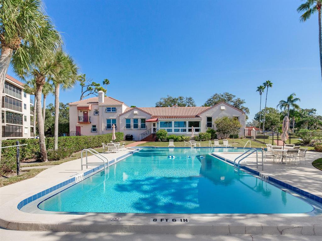 A rectangular swimming pool sits in front of a multi-story building with palm trees — 502 S FLORIDA AVENUE UNIT 124, TARPON SPRINGS, FL