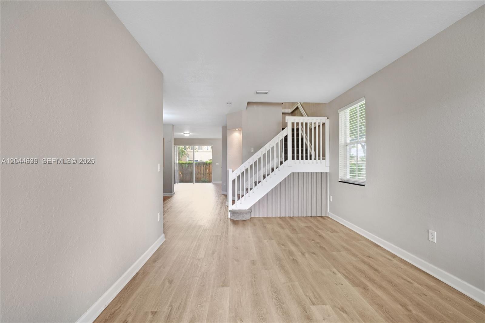 An interior view shows a living area with light wood flooring, beige walls, and stairs — 10709 NW 81st Ln, Doral FL 33178, DORAL, FL