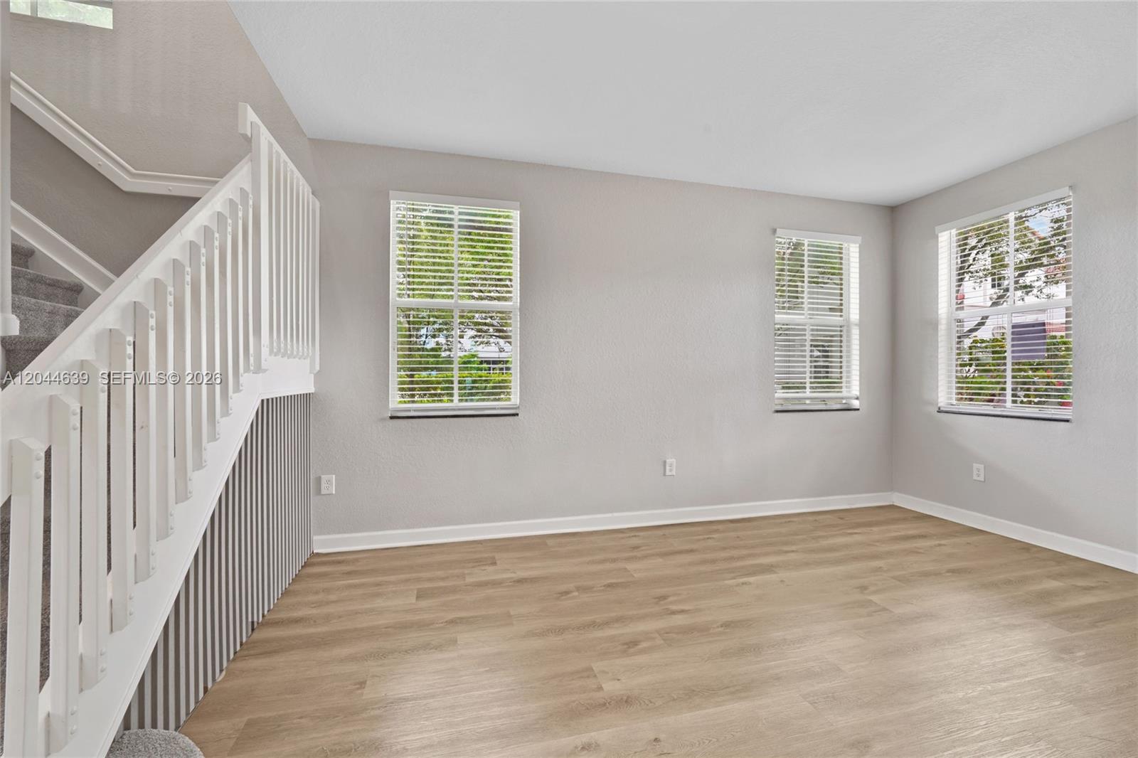 An empty room features light-colored wood-look flooring, gray walls, and a white staircase railing — 10709 NW 81st Ln, Doral FL 33178, DORAL, FL