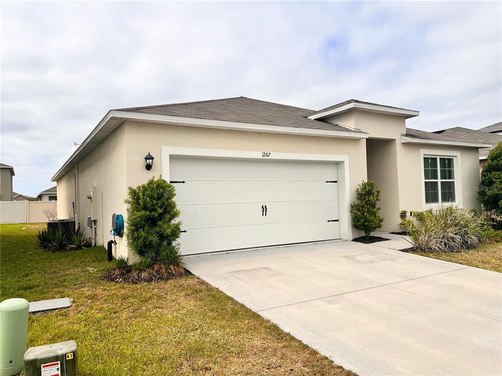 A single-story house exterior features a two-car garage, beige stucco walls, and a concrete driveway — 1267 IGUANA LOOP, DAVENPORT, FL