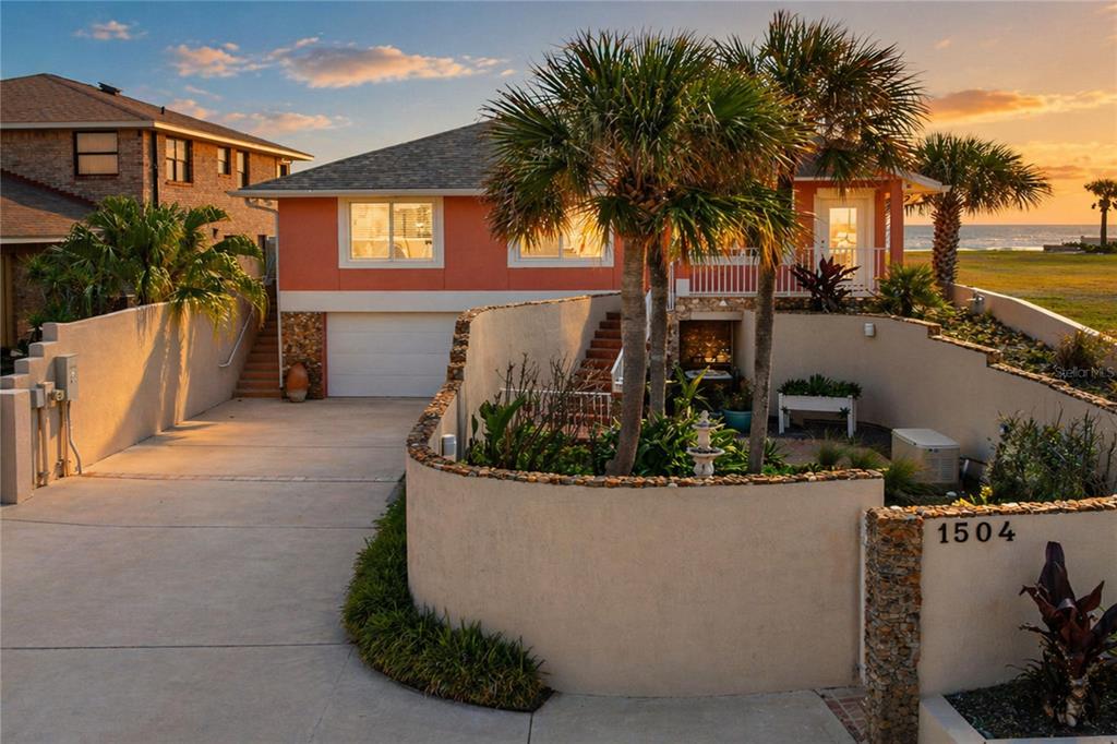 A peach-colored house with a garage and curved stone wall sits near the ocean — 1504 N ATLANTIC AVENUE, DAYTONA BEACH, FL
