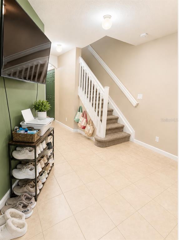 A hallway features a staircase with carpeted steps, a shoe rack, and a wall-mounted television — 2928 HIDDEN HILLS ROAD UNIT 1405, WEST PALM BEACH, FL